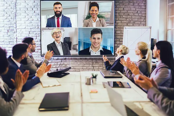 Trabajo híbrido con una persona frente a una laptop mostrando una videollamada con múltiples participantes en una reunión virtual.