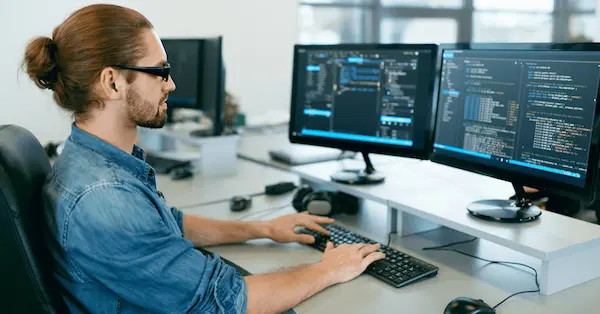 Capacitación en arquitectura de software con enfoque práctico, programador trabajando en código frente a múltiples monitores