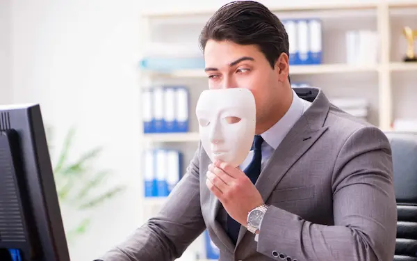 Síndrome del impostor representado por un hombre de negocios con máscara blanca frente al computador.